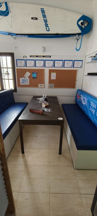 Sala de descanso con mesas y bancos, decorada con elementos de surf.